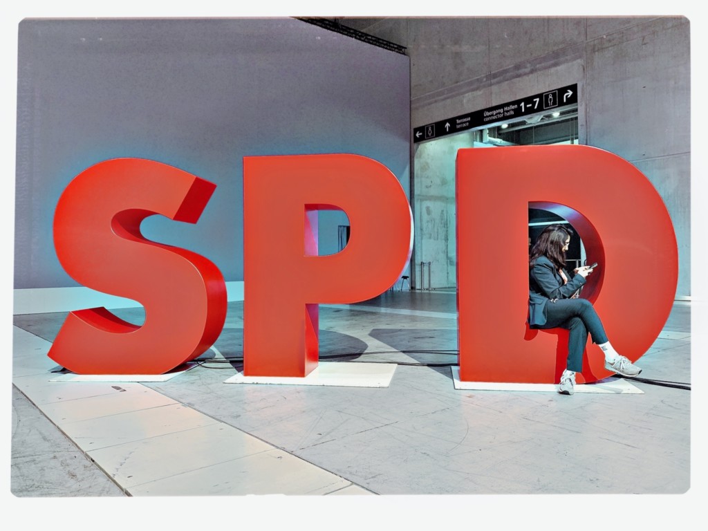 Drei große rote Buchstaben: SPD, im D sitzt eine Person mit ihrem Smartphone